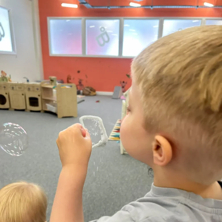 Child blowing bubbles during an indoor nursery activity